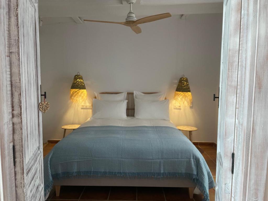 cama con colcha azul, ventilador y lámaparas de noche