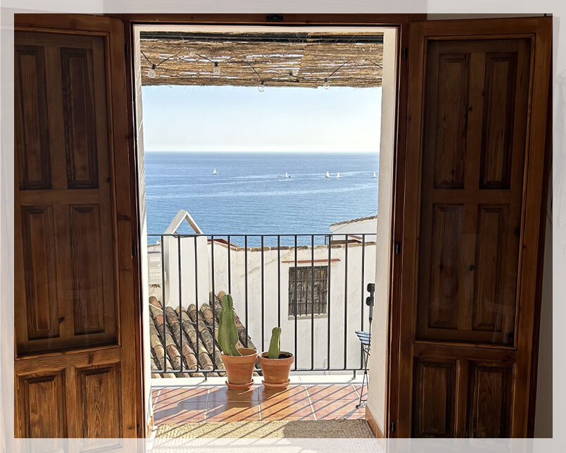 ventanal abierto a balcón con plantas y vistas al mar