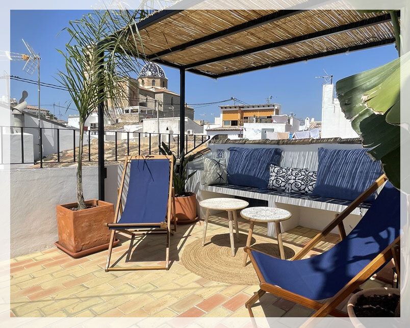 terraza con hamacas plegables azules, banco de obra con cojines de estilo mediterráneo, sombraje y plantas como banano decorativo y areca